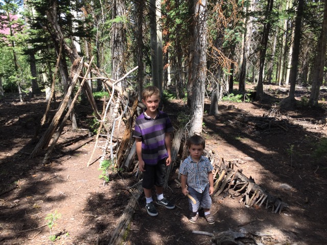 Holland and Beckett, by their hut made of sticks in the woods near the cabin.